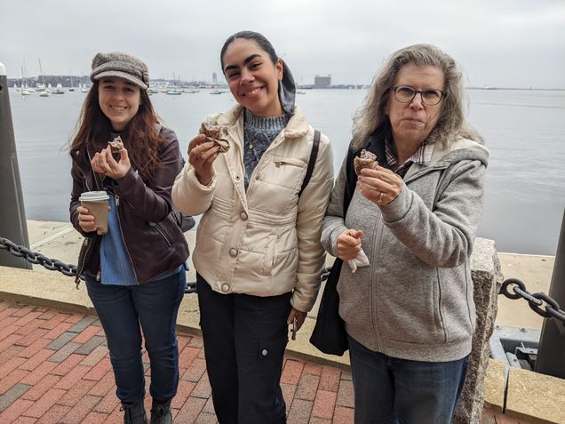 international student and faculty stand in front of the Boston harbor holding donuts